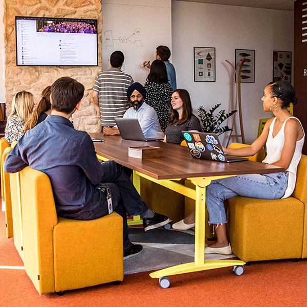 group of nine co-workers collaborating at shared desk and whiteboard