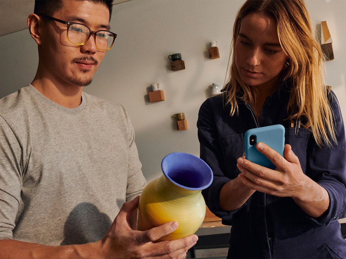 young man holding pottery and young woman with mobile phone engaged in payment transaction