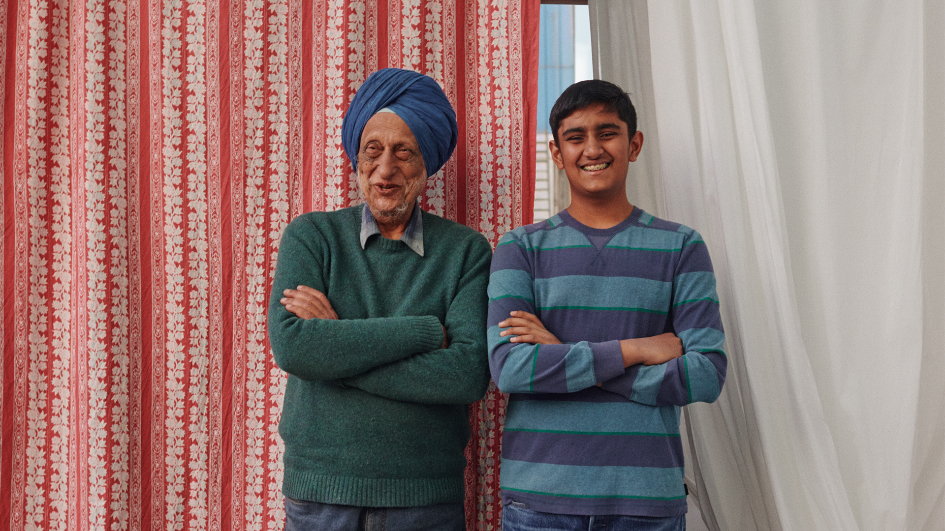 Father and son stand in front of textiles, smiling with arms folded