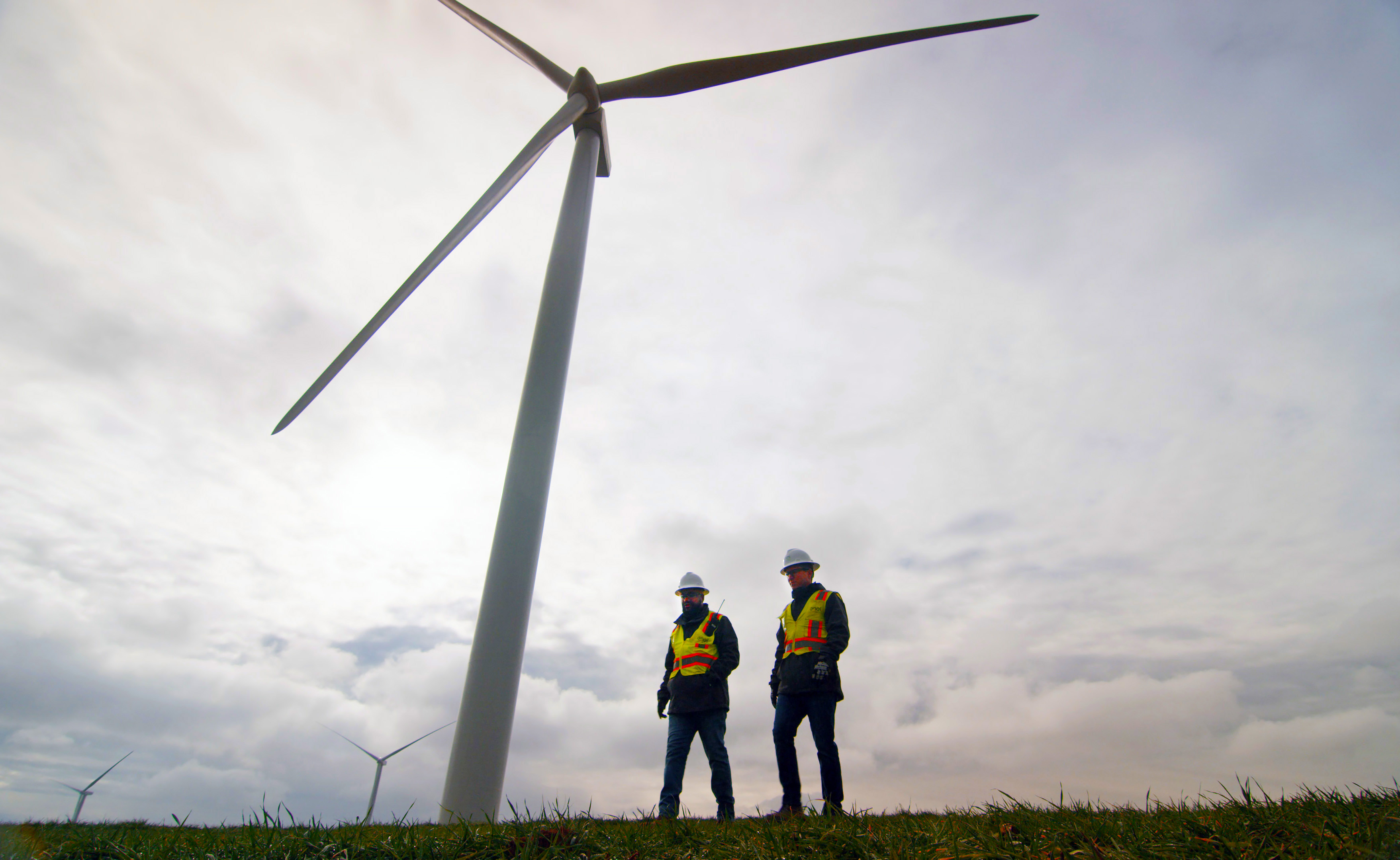 Two wind farm workers under a windmill