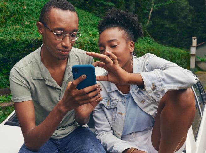 Two people sharing a phone and viewing content on it while sitting outside