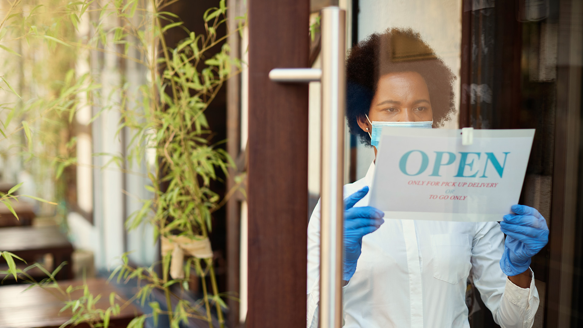 Photo of a woman placing an "Open" sign on the door of a business