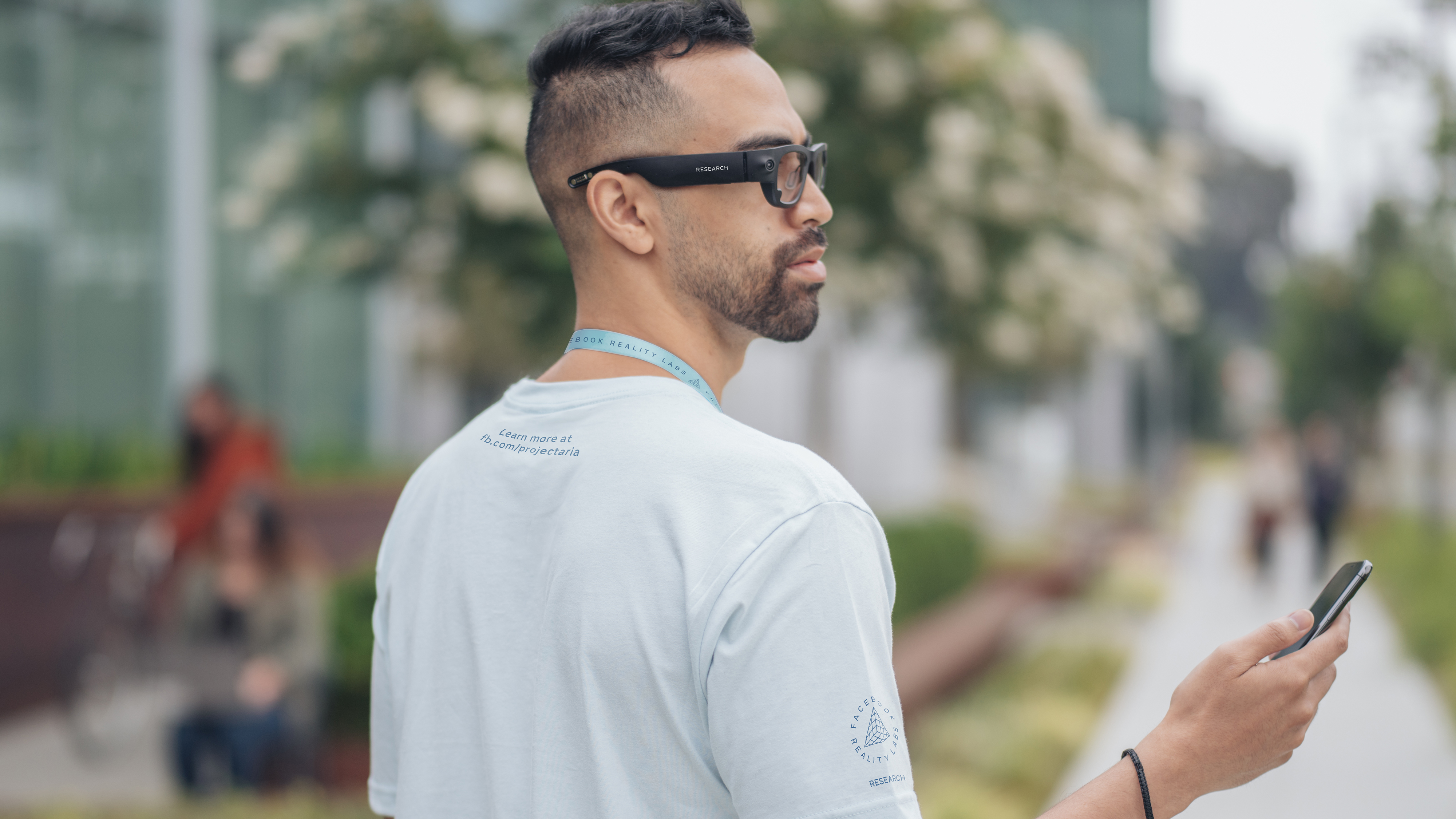 Photo of a Project Aria research participant wearing the device and a t-shirt and lanyard identifying him as a research participant