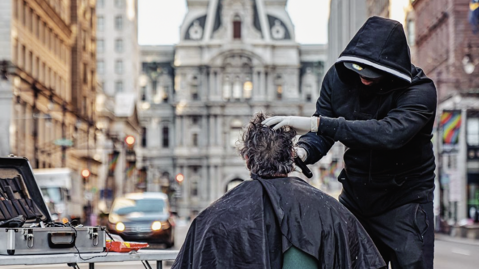Photo of a man giving another man a haircut in the street.