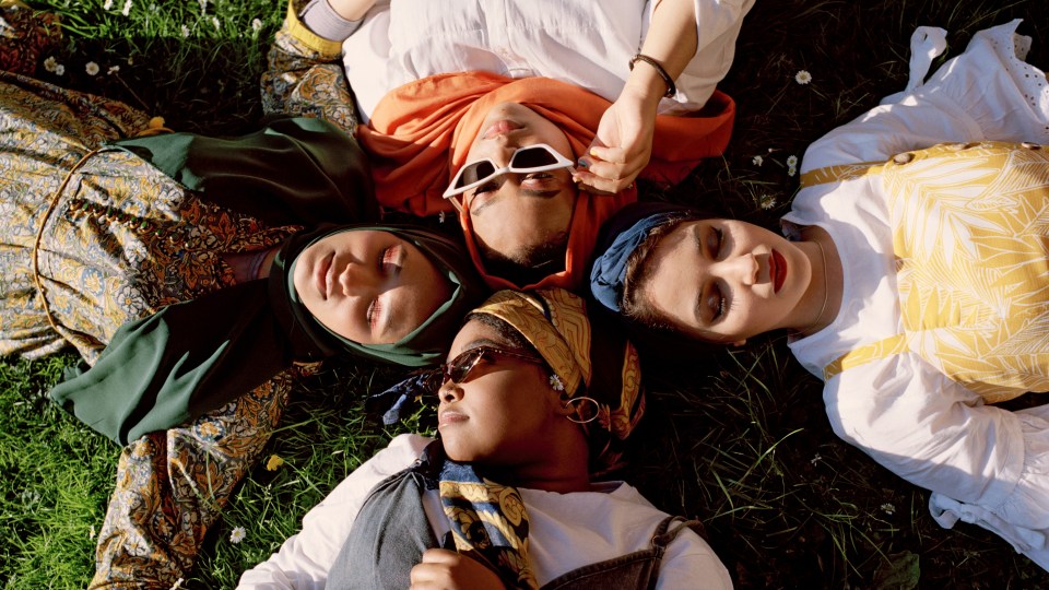 Image of four Muslim women laying on grass