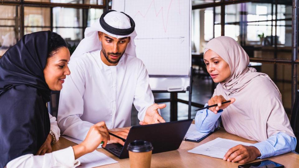 Three people in a business meeting looking at a laptop