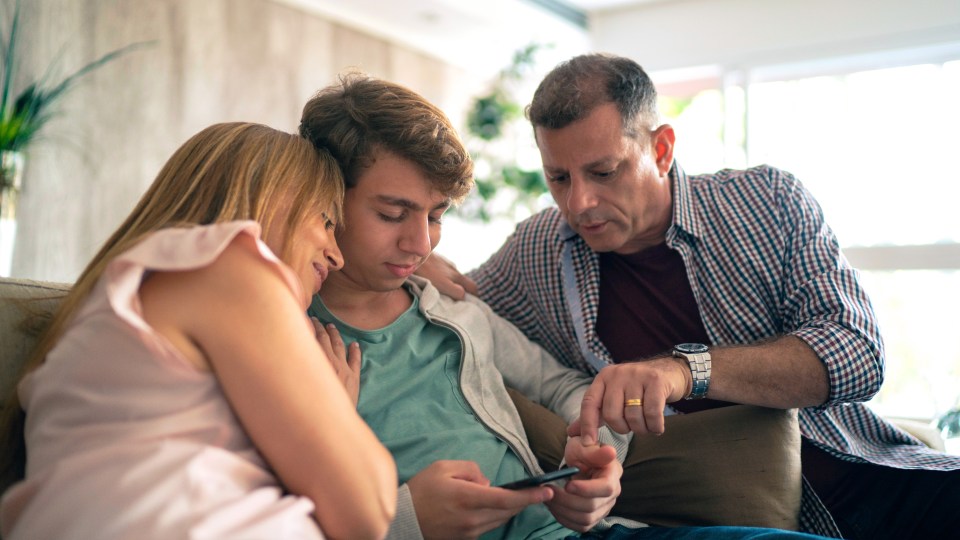 Photo of family sitting on couch and the son looking at his phone