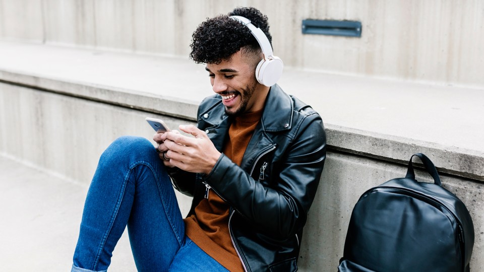 A man sitting down and smiling while listening to music on his phone.