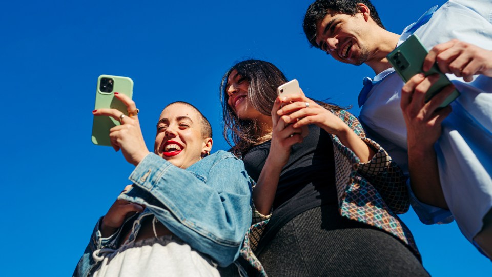 Image showing three friends smiling and looking at their phones.