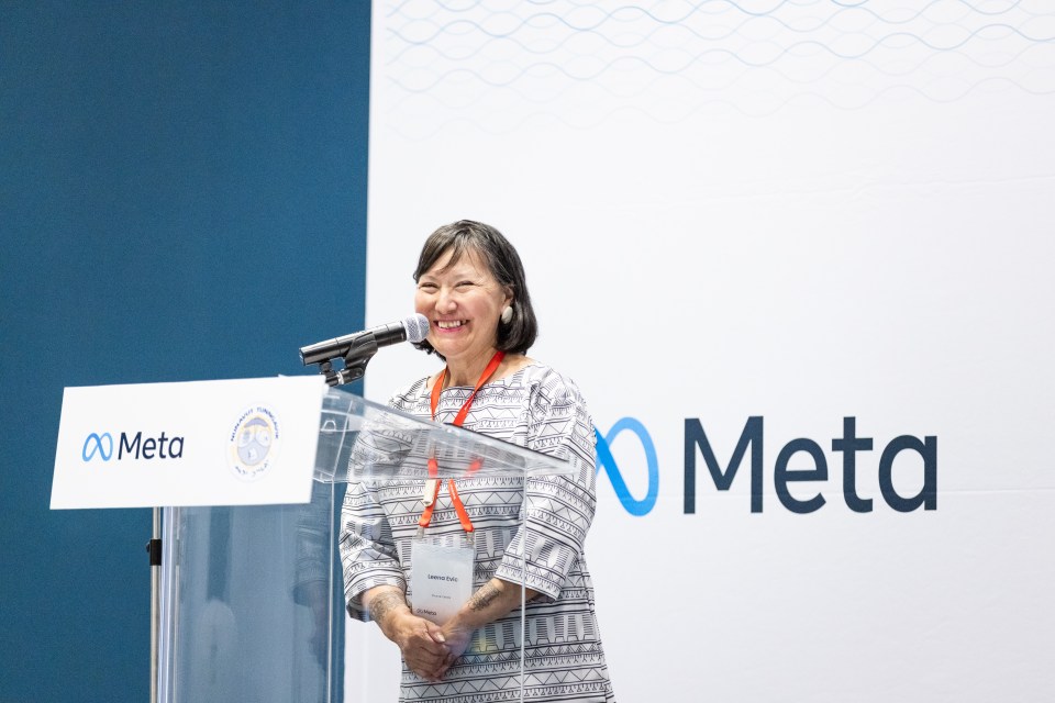 Woman standing on stage in front of a backdrop that says Meta