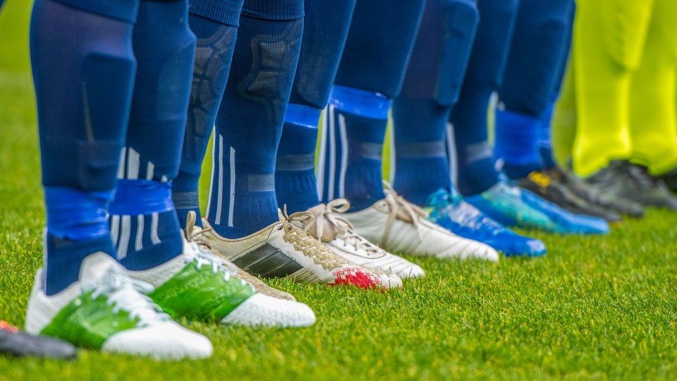 An image showing the cleats of multiple soccer players on a pitch.