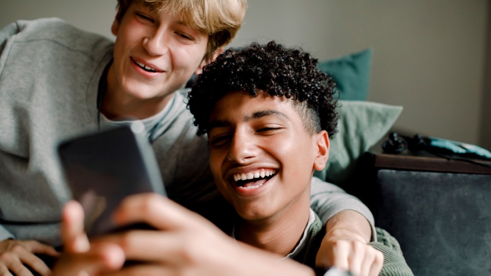 Two teenagers smiling while looking at a phone.