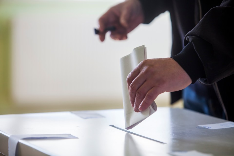 Hand of a person casting a ballot at a polling station during voting.
