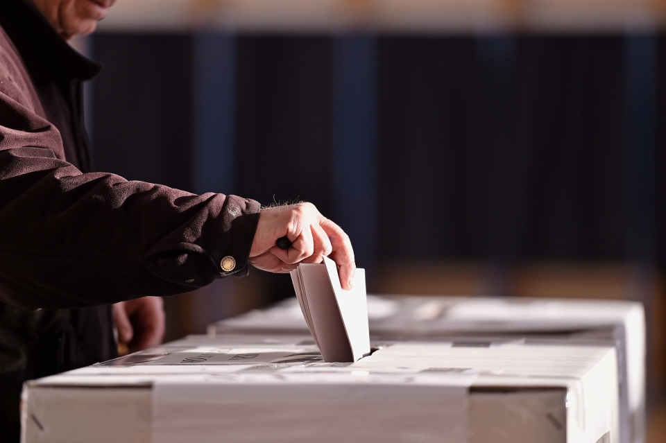 person putting a voting card into a ballot box