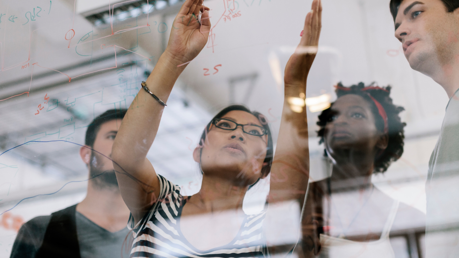 Picture of four people looking at writing on a transparent whiteboard